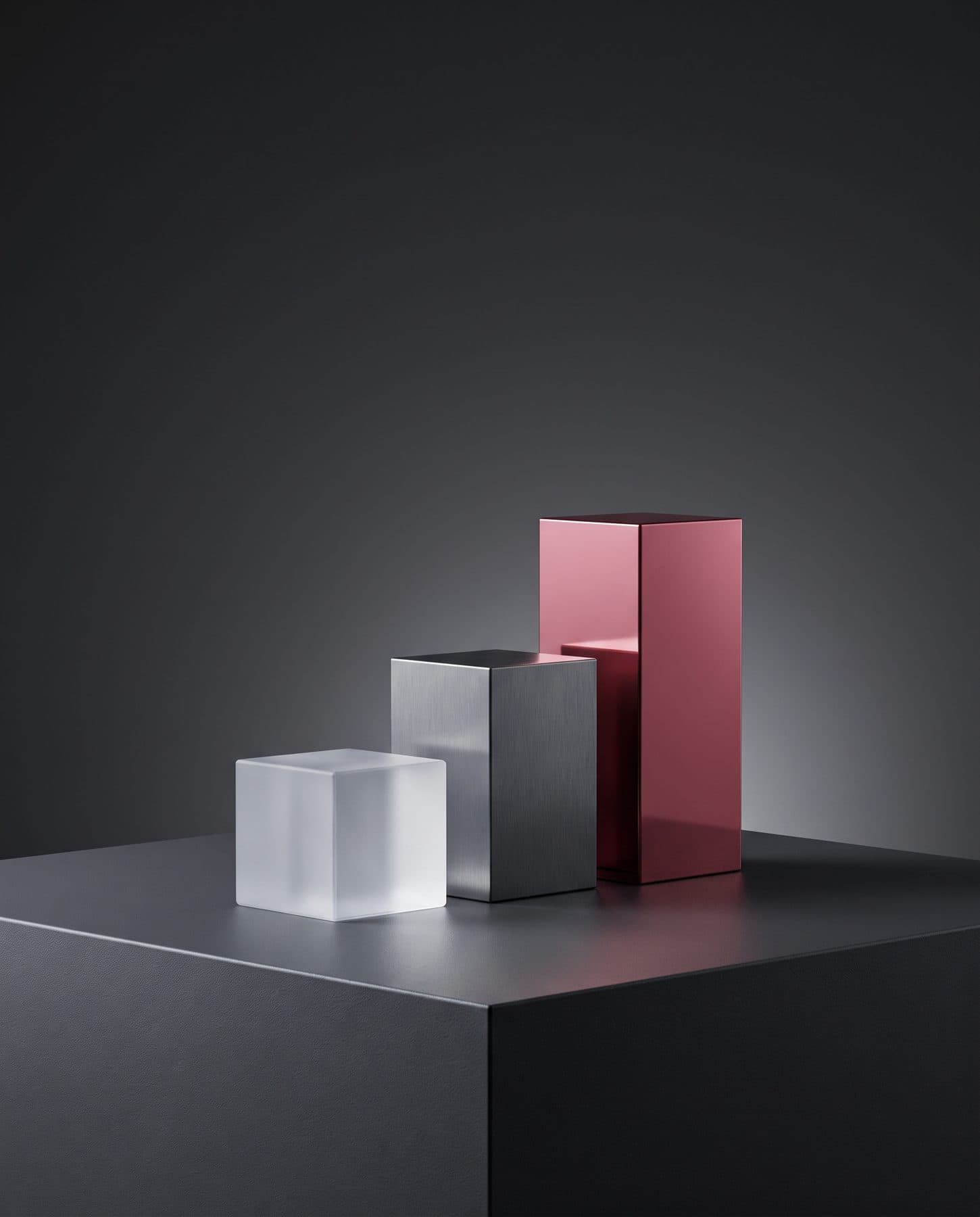 Three blocks of increasing height in frosted glass, graphite metal and rose red